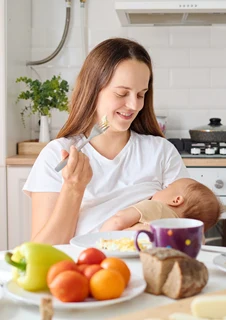 Mamma som ammar sitt barn samtidigt som hon själv äter.