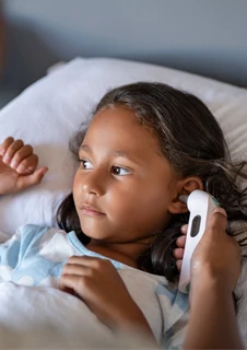 En förälder tar tempen på sitt barn genom en örontermometer för att se om barnet har feber.