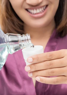 En person häller upp munskölj i en kopp. 