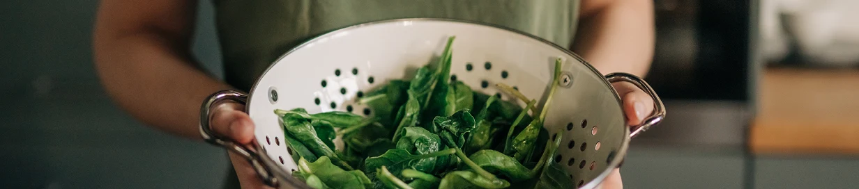 Kvinna i grönt linne håller ett durkslag med nysköljd färsk spenat.