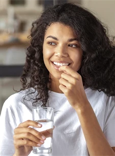 En kvinna tar kosttillskott i samband med ett glas vatten. 