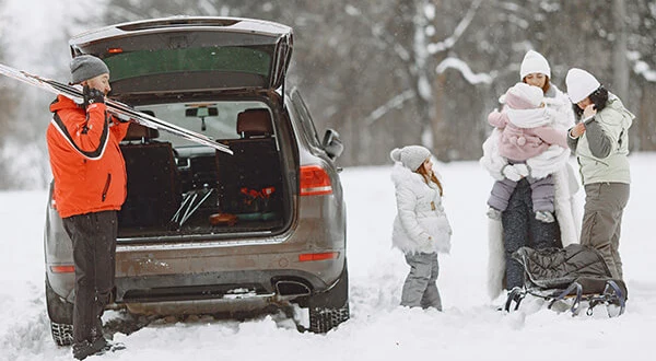 En familj på fem personer packar ur skidutrustningen ur en bil. Runt om är det snö.