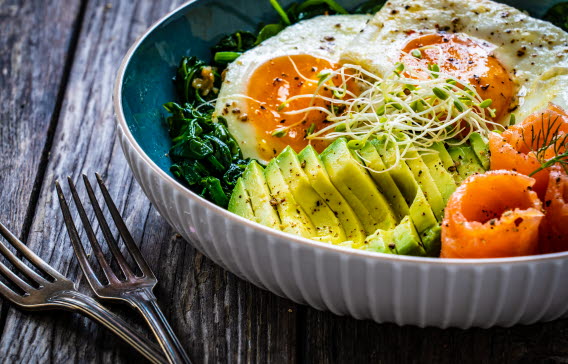 En skål med avokado, rimmad lax och stekta ägg, serverad med två gafflar.