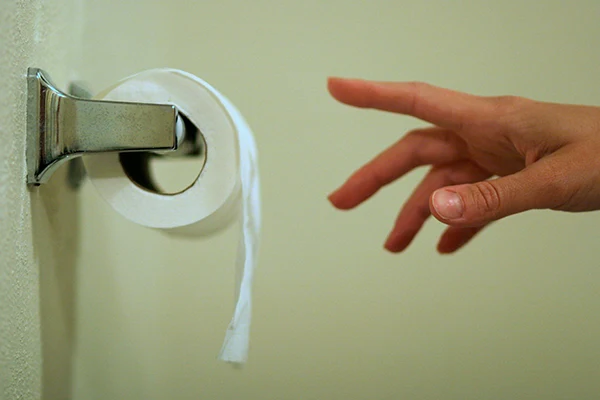 En hand som sträcker sig efter toalettpapper. 