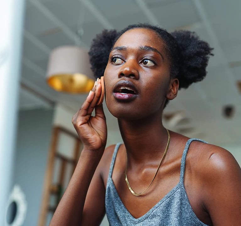 En kvinna applicerar hudvård samtidigt som hon tittar sig själv i en spegel. 