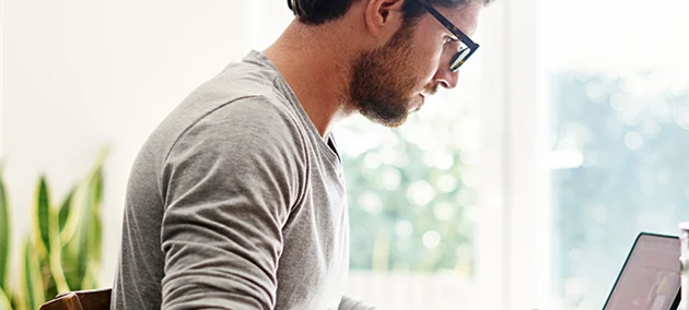 En man sitter i ett kök, äter frukost och tittar på en ipad.