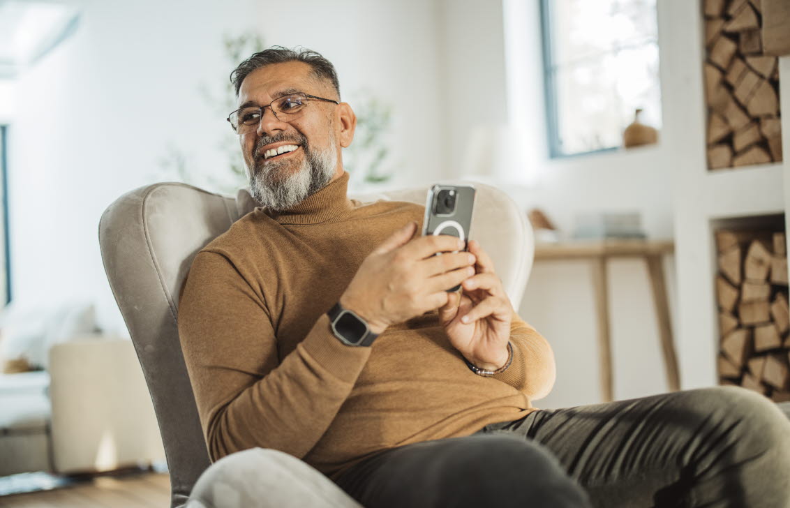 En man sitter i en fåtölj med en mobil i handen.
