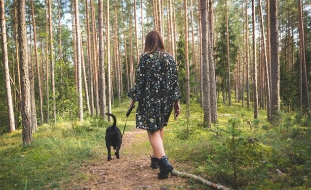 En kvinna går med en hund i skogen.