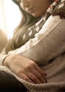 En kvinna sitter i en soffa och håller båda armarna om magen.