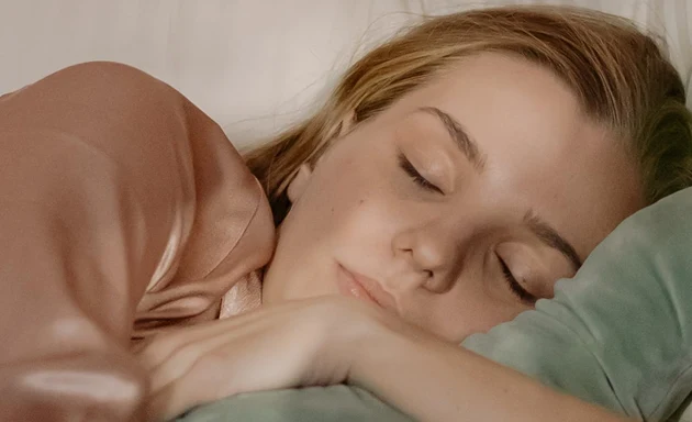 En kvinna som sover i sin säng och kramar om ett gossedjur. 