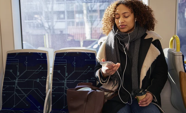 En kvinna sitter på tunnelbanan och tittar ner på sin mobil.