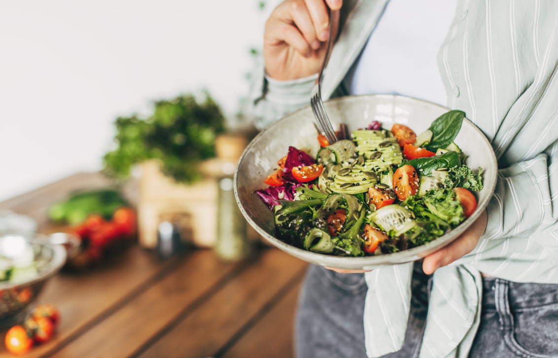 Kvinna håller i en skål med sallad med grönsaker och baljväxter, lämplig för personer med typ 2-diabetes.