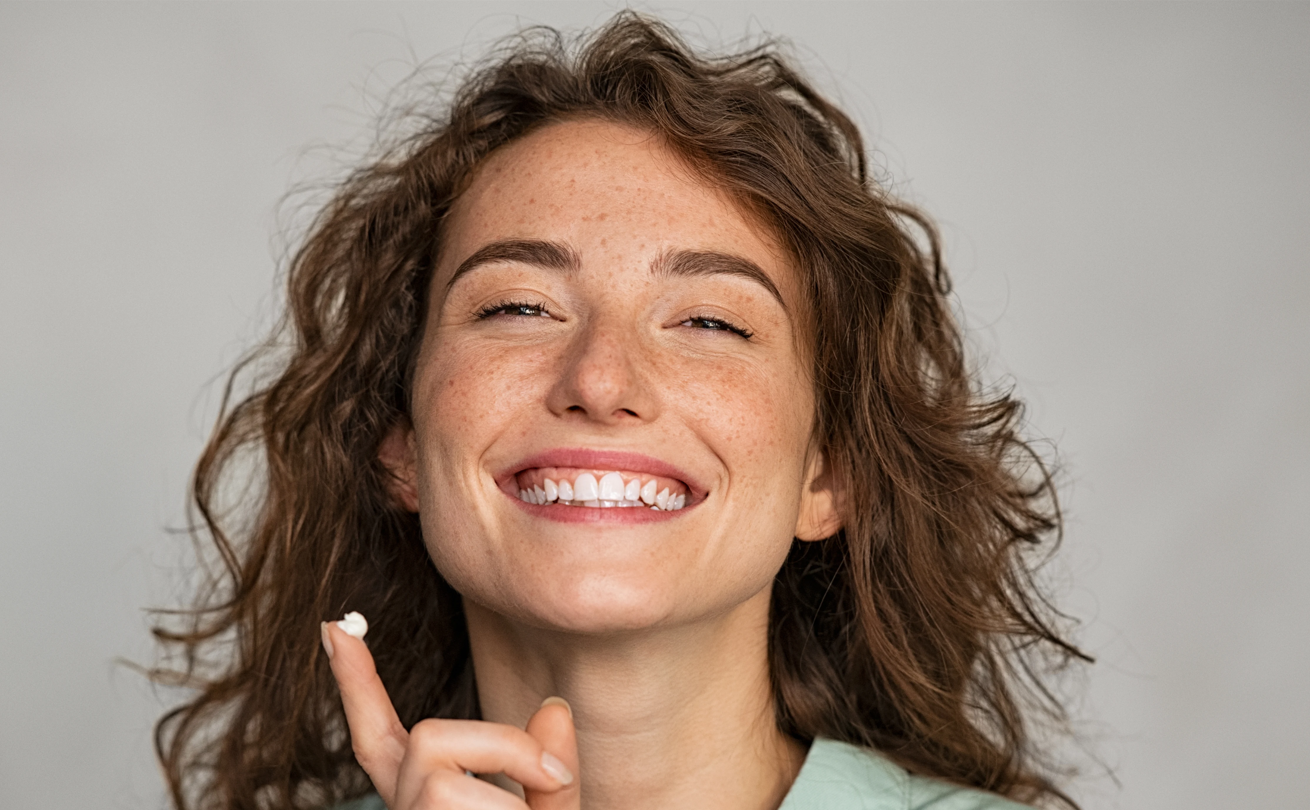 En glad kvinna håller i en hudvårds-produkt, hon har en klick produkt på sitt ena finger. 