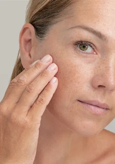 En kvinna som håller ena handen för kinden med hudvård och lätt makeup applicerad på huden