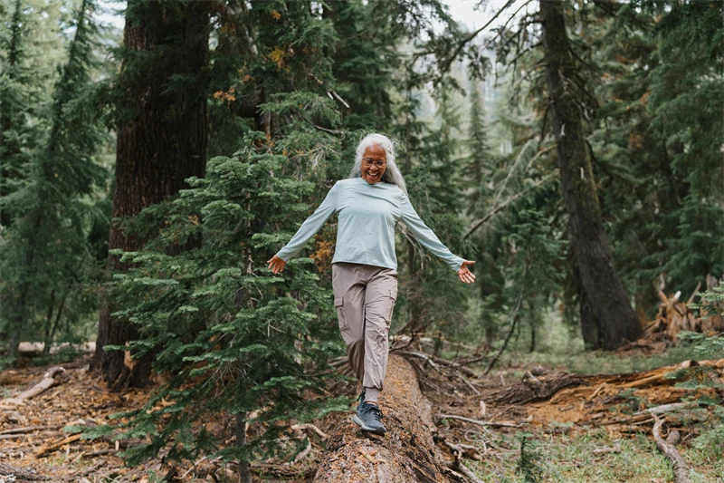 En glad medelålders kvinna balanserar på en stock i skogen