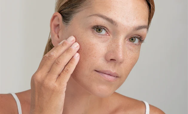 En kvinna som håller ena handen för kinden med hudvård och lätt makeup applicerad på huden