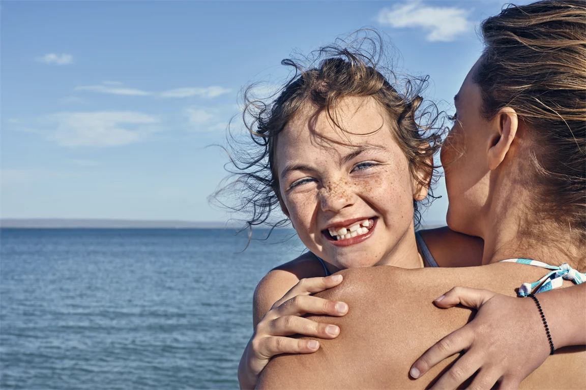 Glad flicka kramar mamma på stranden.