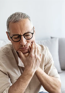 En man med tandvärk håller händerna över ena käken. 