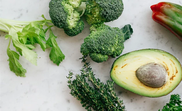 Avocado, broccoli och andra grönsaker ligger på ett bord.