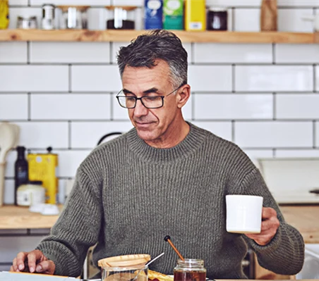 En man sitter i köket, äter frukost och dricker kaffe.