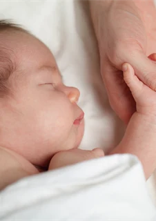 Liten sovande bebis med RS-virus som håller sin mammas hand.