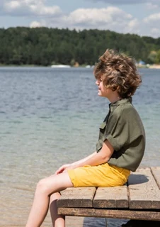 En pojke sitter på en brygga och tittar ut över en sjö under en sommardag. 