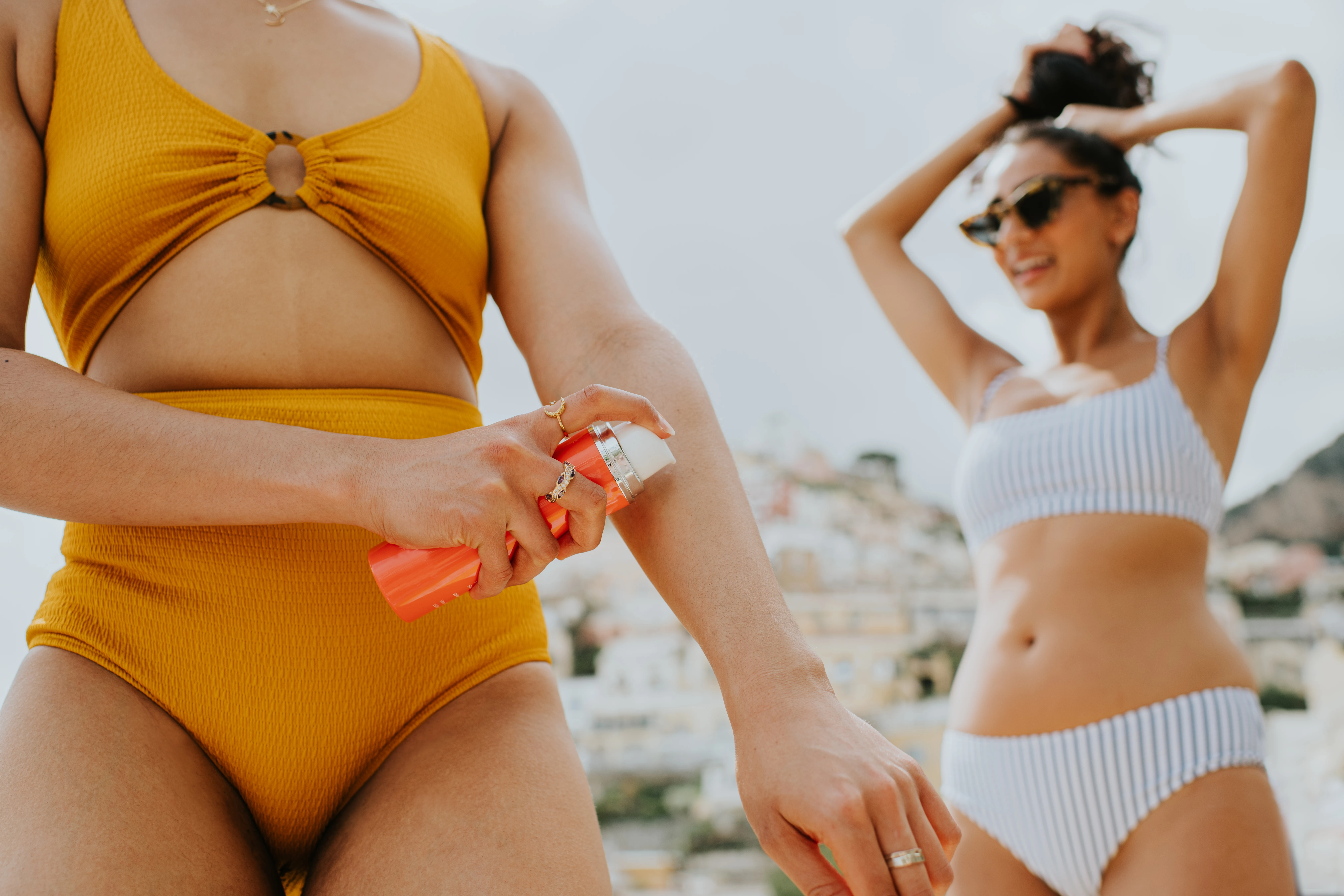 Två kvinnor i bikini smörjer in sig med solskydd.