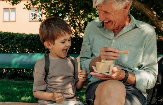 En glad morfar äter glass tillsammans med sitt barnbarn på en parkbänk.