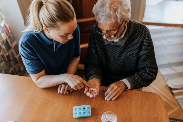 En sjuksköterska hjälper en äldre man med hans medicin