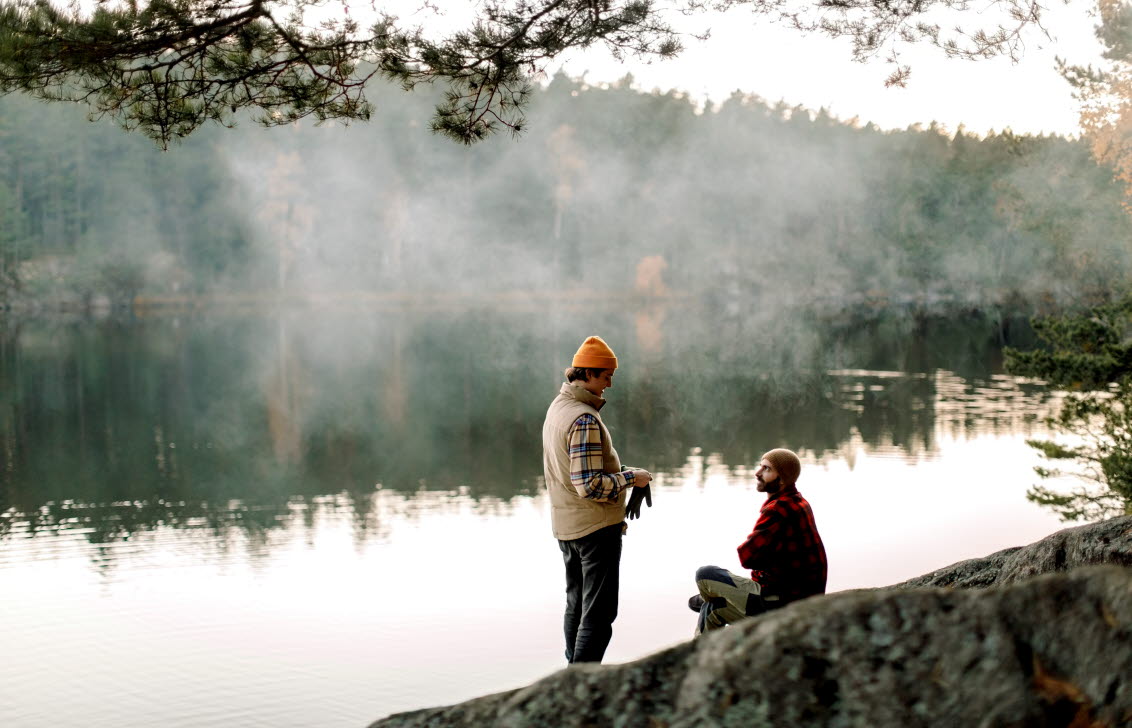 Två män pratar på en klippa vid en sjö en dimmig morgon.