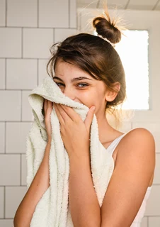 En ung kvinna torkar försiktigt av ansiktet med en handduk efter att hon tvättat det. 