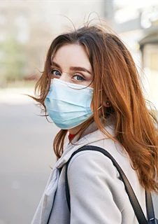 En kvinna med munskydd som står på en gata.