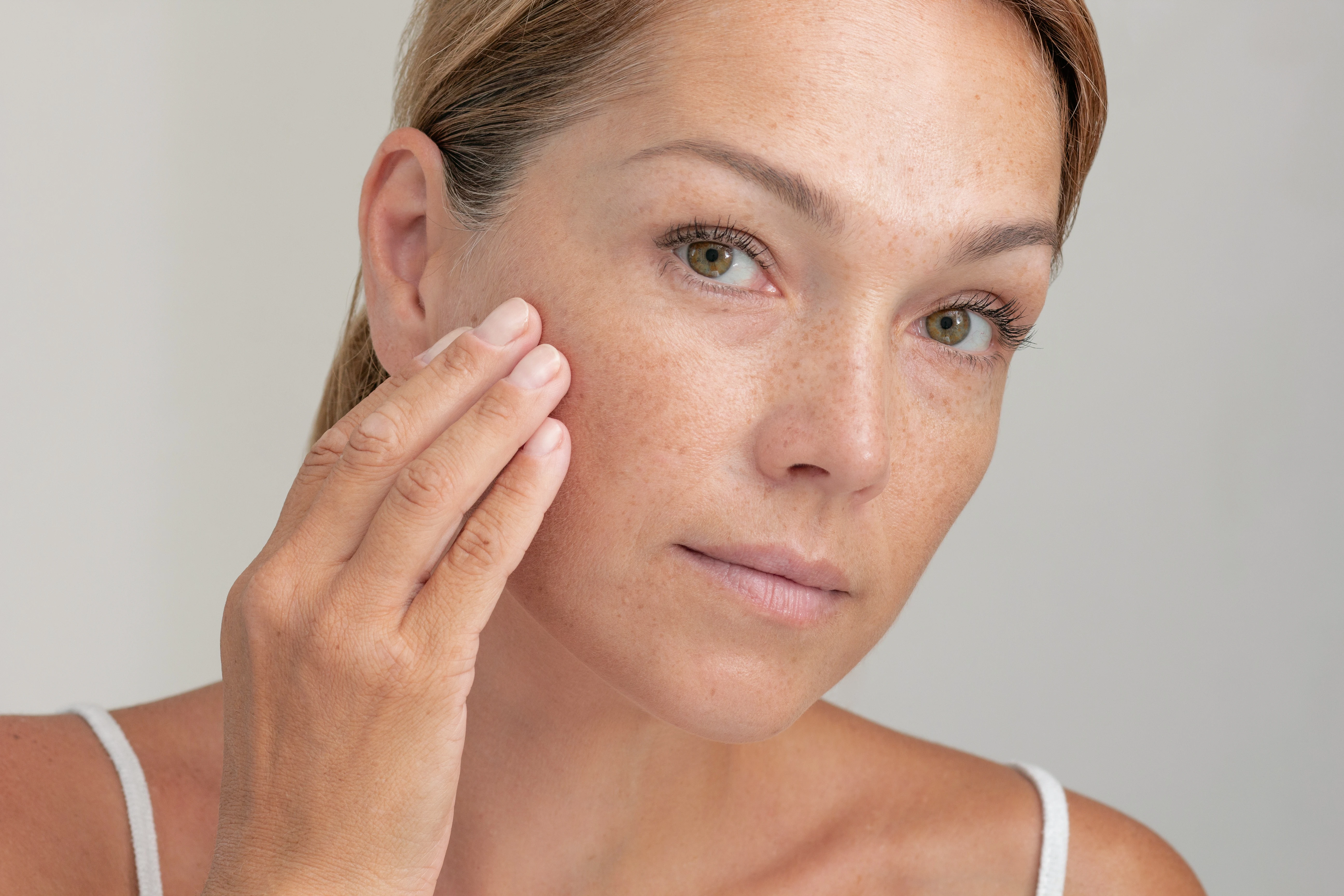 En kvinna som håller ena handen för kinden med hudvård och lätt makeup applicerad på huden