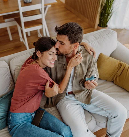 Ett ungt par sitter tillsammans i en soffa medan en av dem håller i en inhalator.