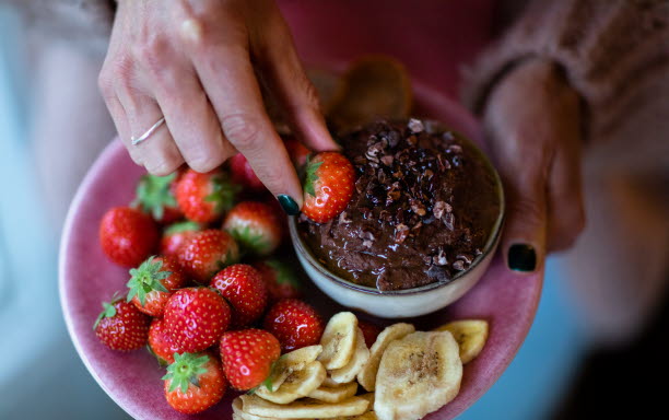 Ett fat med jordgubbar och bananskivor som doppas i en skål med chokladhummus.