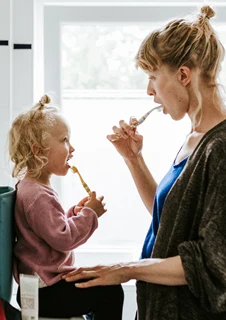 En mamma och ett barn borstar tänderna tillsammans i ett badrum. 