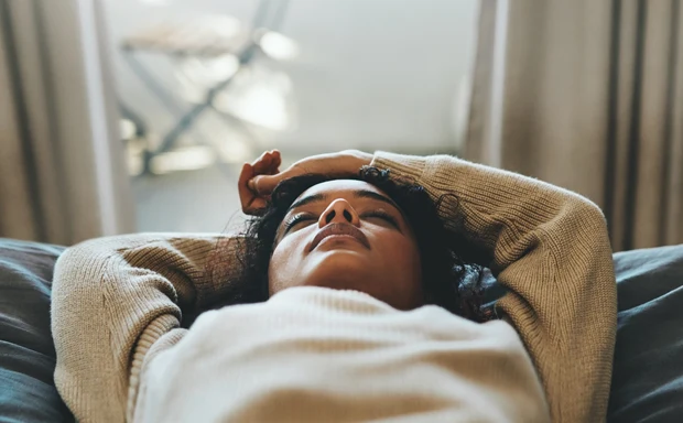 En kvinna ligger i en säng med händerna ovanför huvudet. 