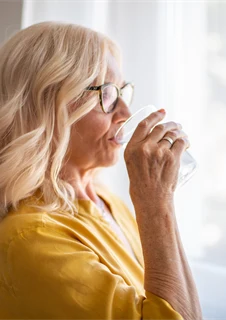 Kvinna med kronisk, långvarig hosta som dricker ett glas vatten för att lindra.