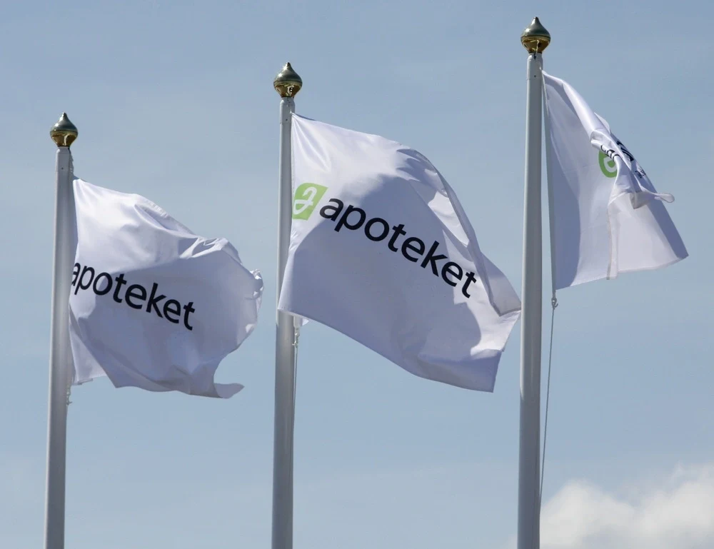 Tre flaggstänger med Apotekets flaggor som vajar i vinden. 