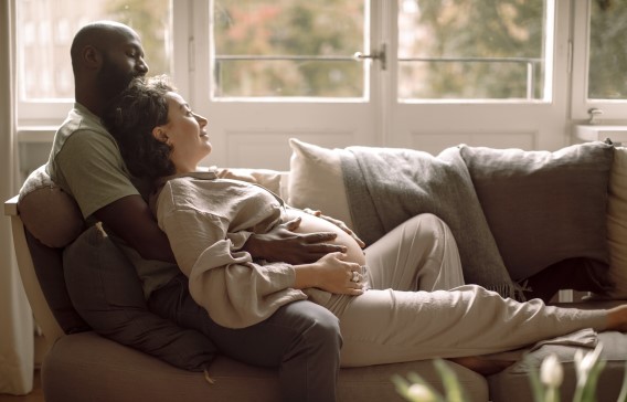 En man som omfamnar sin gravida partner medan de vilar tillsammans i soffan hemma