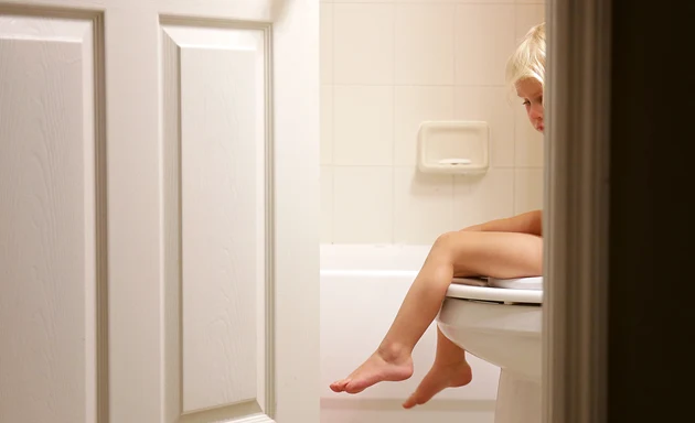 En skymt av ett barn syns bakom en vägg när hen sitter på toaletten.