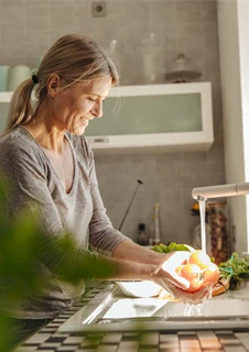 En kvinna som står och sköljer av grönsaker i köket.