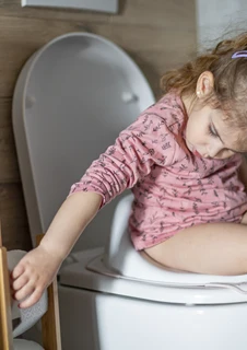 Ett barn sitter på en potta och sträcker sig efter toalettpapper. 