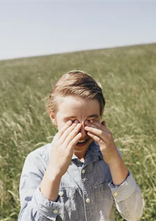 Pojke med gräsallergi som kliar sig i ögonen på en äng.