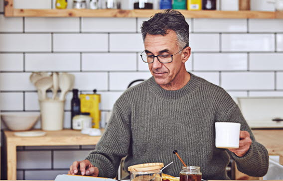 En man sitter i köket, äter frukost och dricker kaffe.