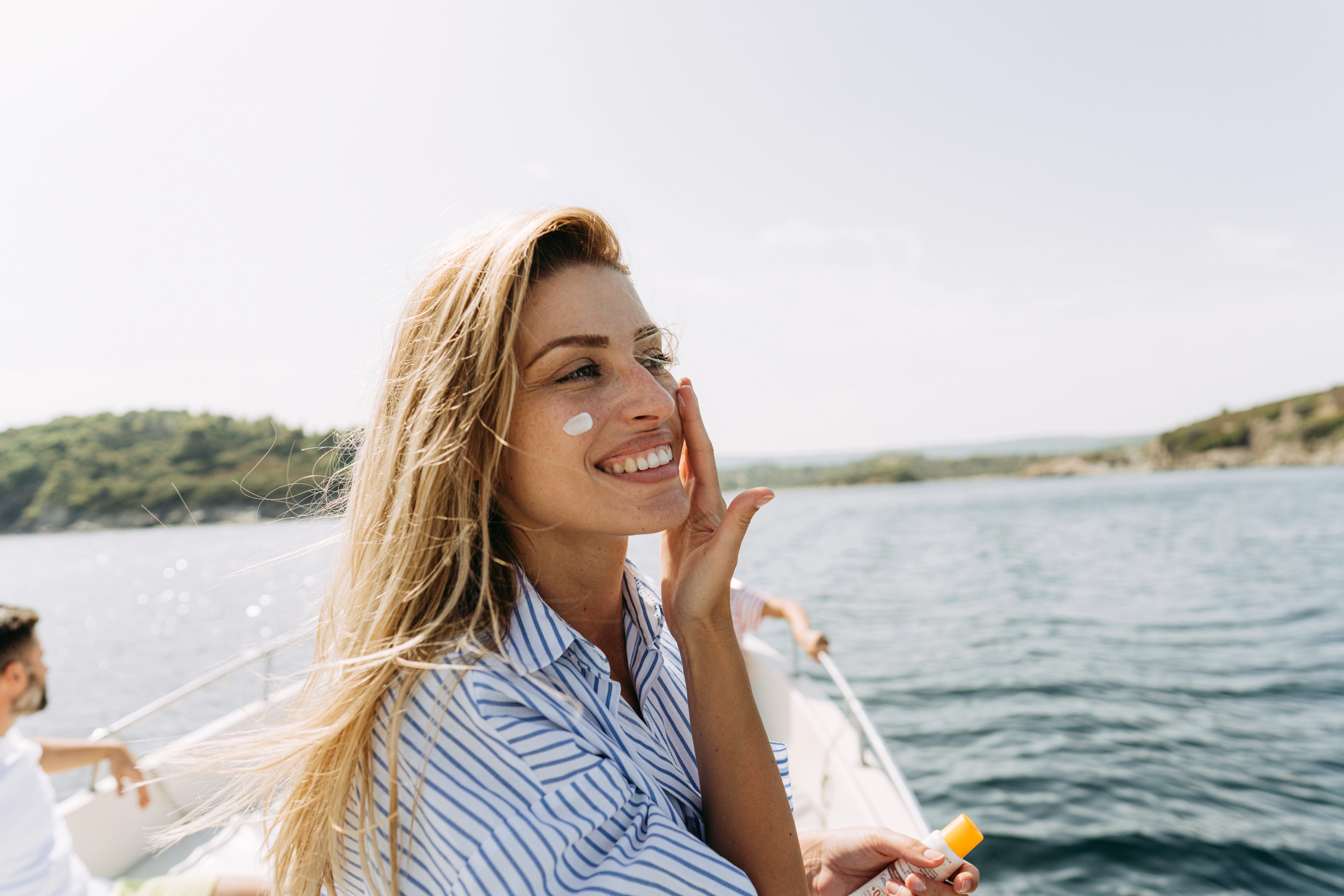 En kvinna står på en bår och smörjer in sgi med solskydd i ansiktet för att skydda sig mot solen.