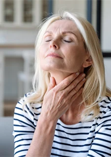 Kvinna med halsont som tar sig på halsen.