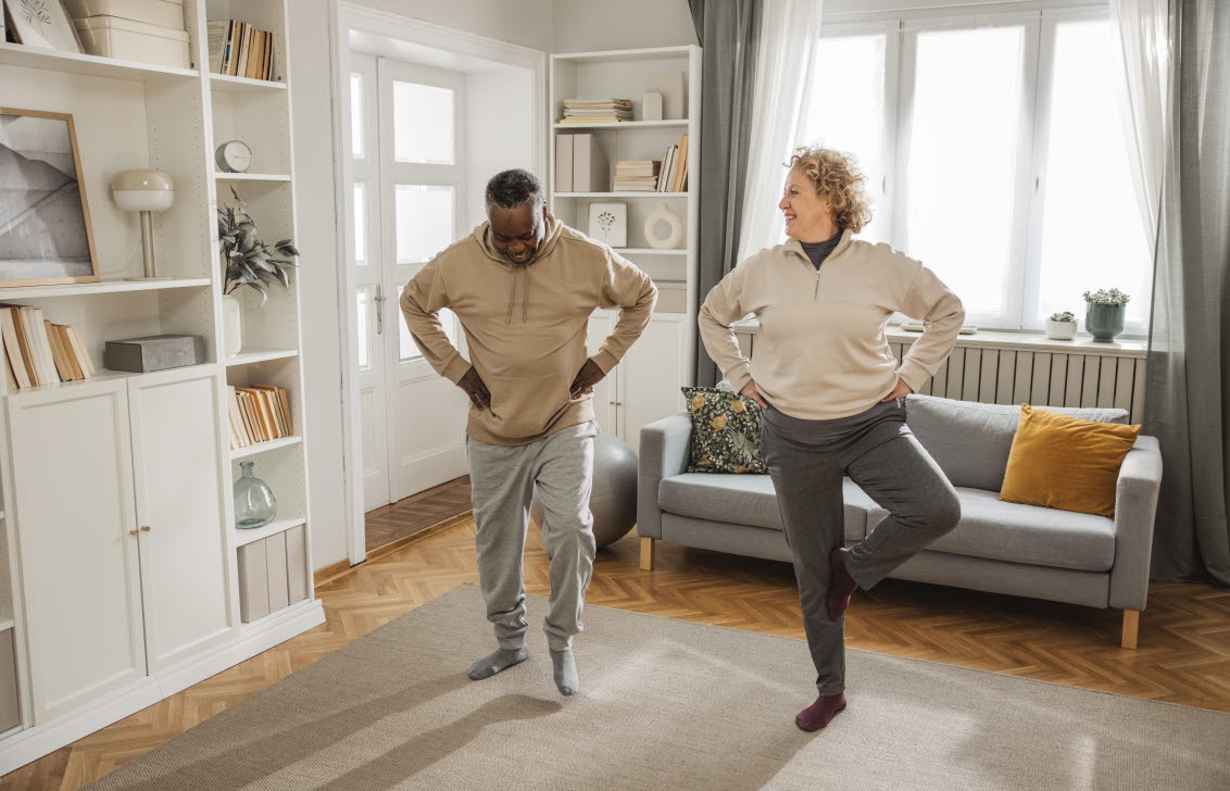 	Två person står på ett ben i vardagsrummet för att öva upp balansen.