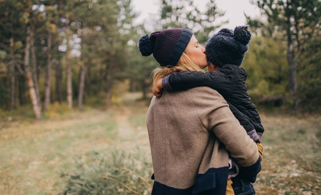 En mamma som pussar sin son på kinden ute i naturen.