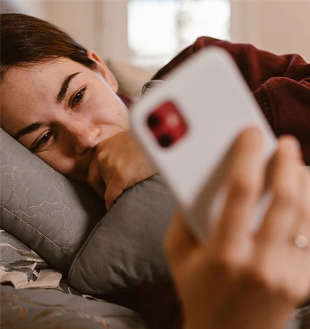 En kvinna ligger i en soffa och tittar på sin mobil.